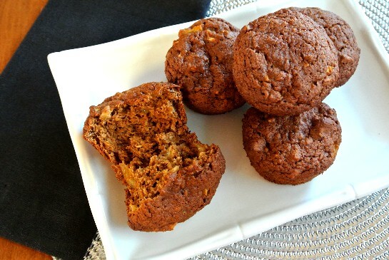 Apple Granola Muffins have a photo taken from above. Five muffins on a white rectangle plate with one muffin broken open.