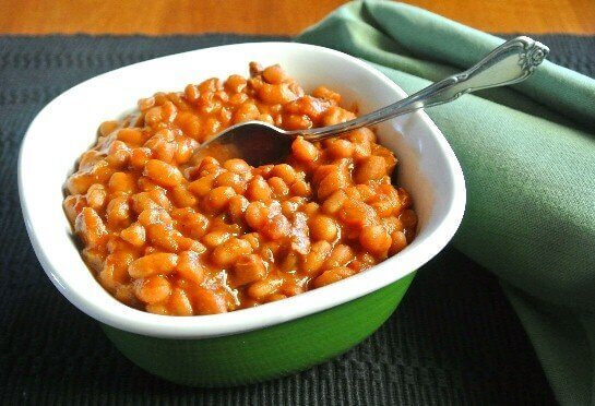 BBQ Baked Beans in the slow cooker are being spooned up in a green and white bowl.