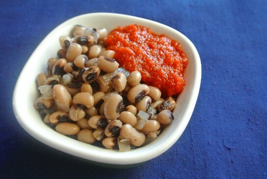 Slow Cooker Black Eyed Peas are in a singles erve dish with a dollop of bright red Caribbean Sauce.