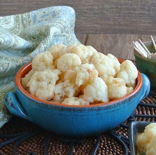 Mildly Marinated Cauliflower is piled high in a turquoise handled pottery bowl with toothpicks on the side.