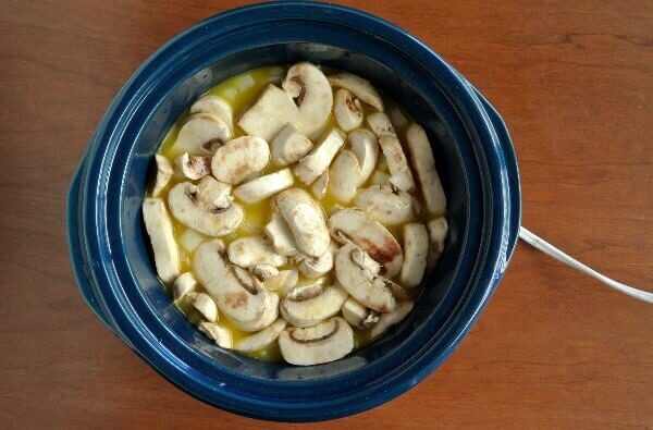 Healthy Slow Cooker Mushrooms and Rice are sliced and piled into a crockpot. Overhead view looking down into a cobalt blue crockpot.