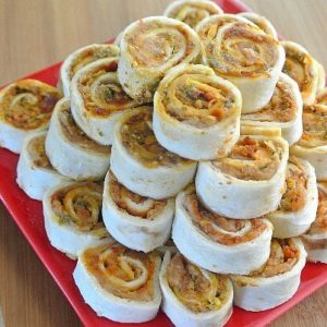 Pesto Tortilla Rollups are stacked like a pyramid on a red square plate.
