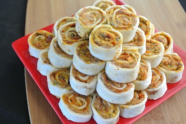 Appetizer pinwheels are stacked like a pyramid on a red square plate.