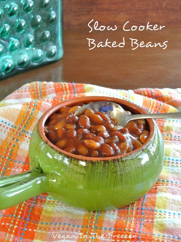 A green handled bowl if fill with baked beans on a plaid napkin.