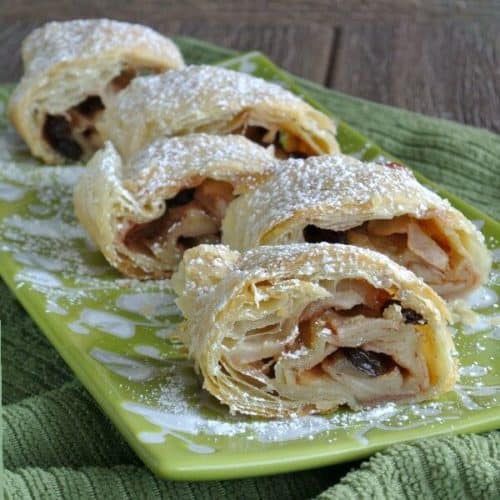 A row of staggered thick slices of apple strudel are sprinkled with powdered sugar.