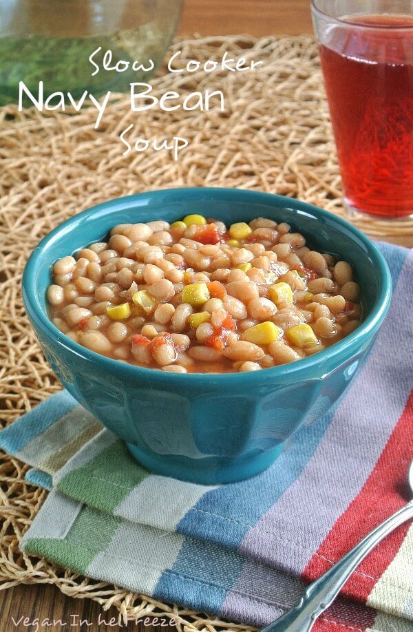 Slow Cooker Navy Bean Soupis in a turquoise bowl and on a colorful striped napkin including turquoise. The navy beans are waiting for you to take a big bite.