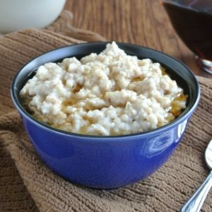 Slow Cooker Irish Oatmeal is filling a blue porcelain bowl with maple syrup floating on top. Spoon on the side.