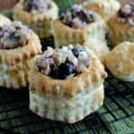 Vegan Puff Pastry Appetizer is photographed with filled pastried lined up on a black cooling rack. They are sitting on a green mat.