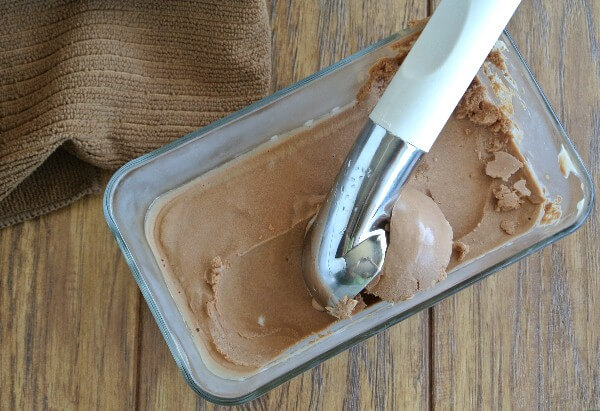 Scooping out a big scoop of chocolate ice cream from a glass container.