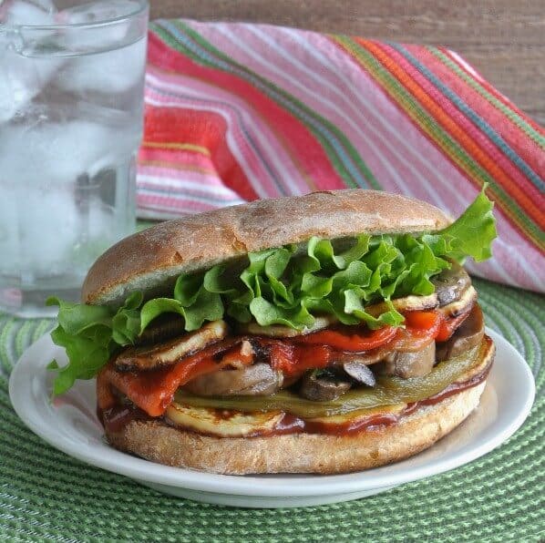 Stack of roasted vegetables on a wide bun and sitting on a white plate and a green mat.