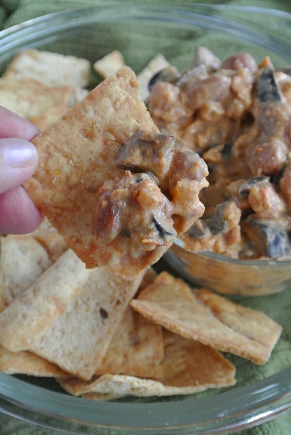 A scoop of dip on a chip is being help close to the camera for a close look of creamy rich brown dip with lots of texture.