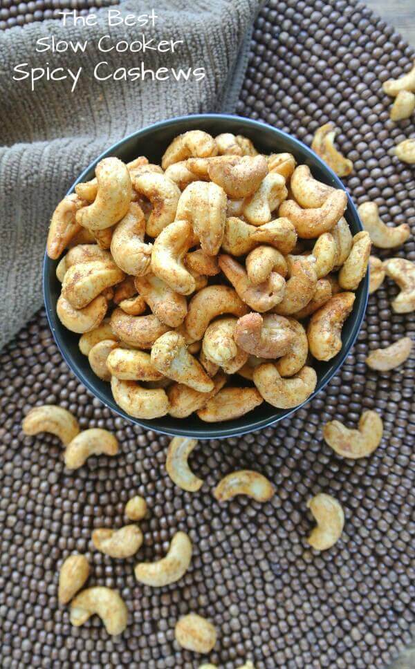 Overhead photo of  spice covered cashews verflowing from a bowl on to a chocolate covered woven mat.