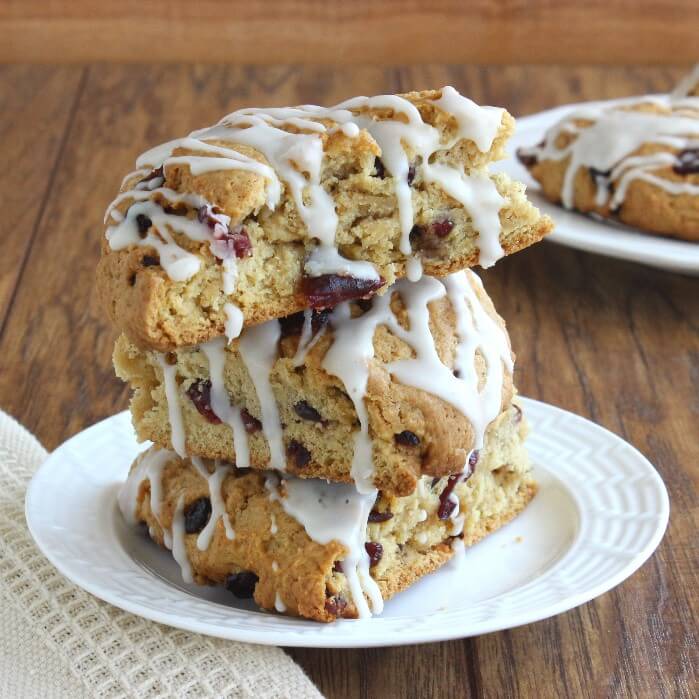 Three Cranberry Orange scones stacked on top of each other on a small white plate.
