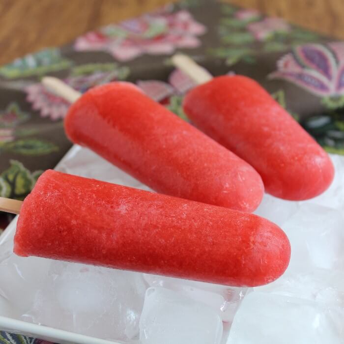 Three apple strawberry popsicles and a side view of them laying on a bed of ice and a white plate. 
