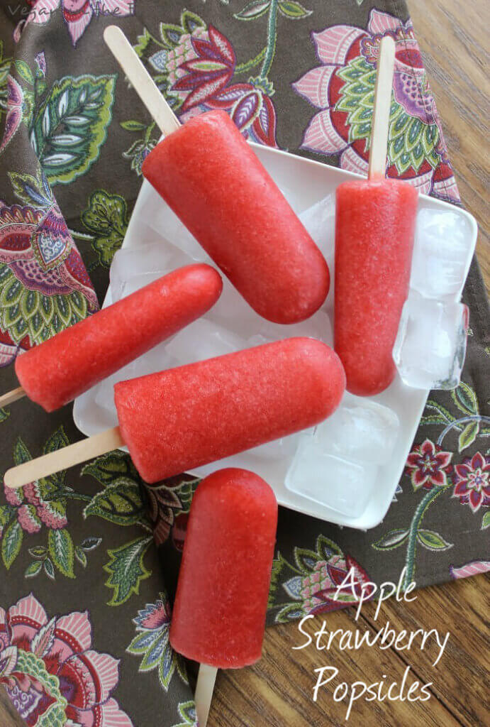 Five apple strawberry popsicles laying on a bed of ice and a square white plate.