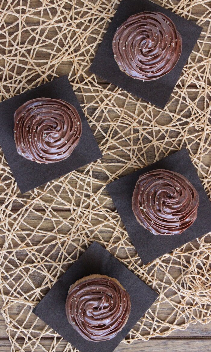 Overhead view of four frosted desserts on dark brown napkins and a beige woven mat.