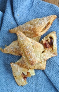Overhead photo of triangle shapped turnovers with some broken open to show the apples and berries inside.