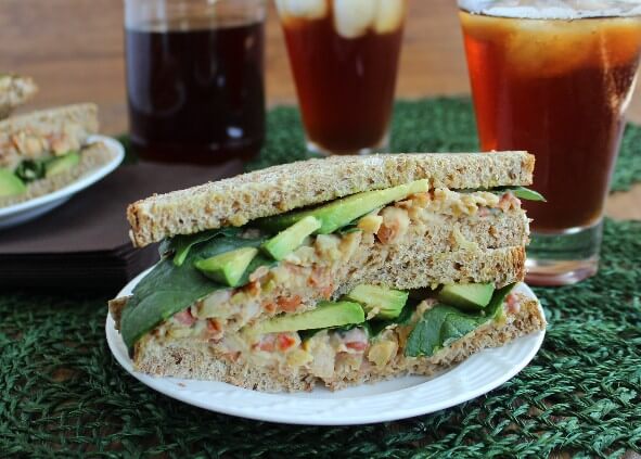 Two sandwich slices are stacked on top of each other with the chickpea salad and avocado slices showing clearly.