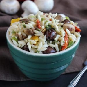 Small orzo pasta is tossed with olives and mushrooms and served in a green bowl.