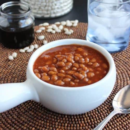 Front angled view of baked beans in a bowl with a spoon on the side.
