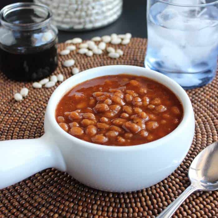 Front angled view of baked beans in a bowl with a spoon on the side.