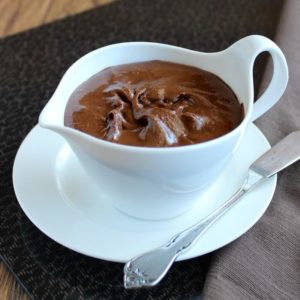 Homemade Nutella is a chocolate-hazelnut spread that is fillinf a white creamer with a spreading knife on the side.