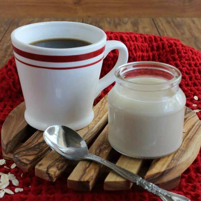 A cup of coffee in a retro white and red mug is sitting alongside a jar of creamer.