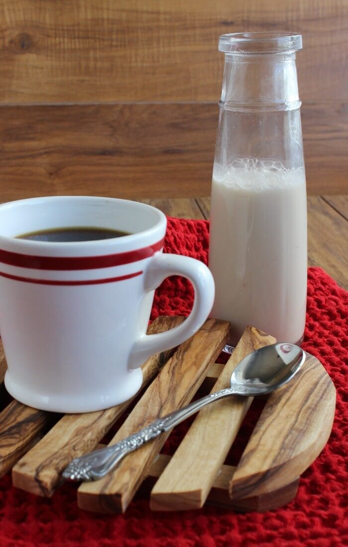 A small old fashioned milk bottle is holding creamer and it's nest to a cup of coffee.