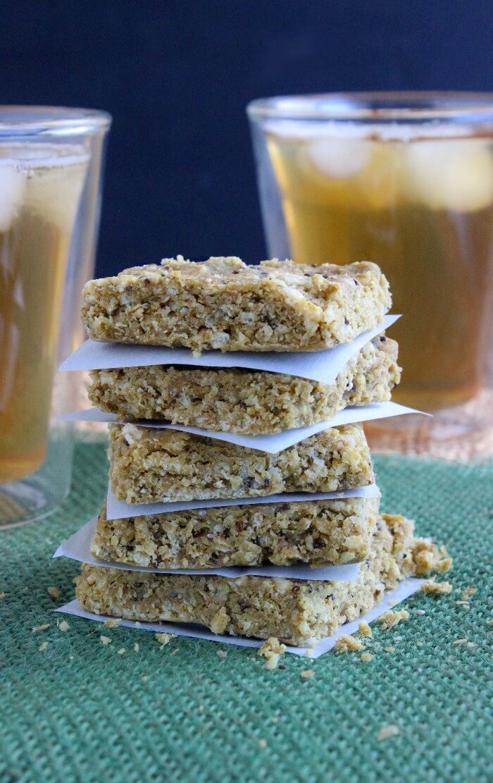 Four protein squares are stacked with parchment papersquares in between each treat. They are sitting on a green mat with iced tea behind.