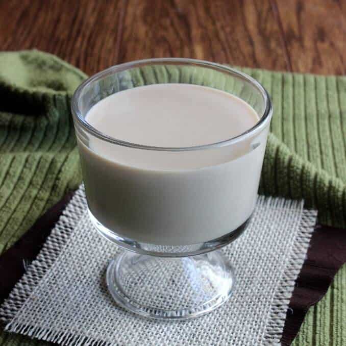 White creamy milk in a small clear glass footed glass.