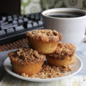 Cinnamon Streusel Mini Muffins are stacked three high on a white plate with streusel all around.