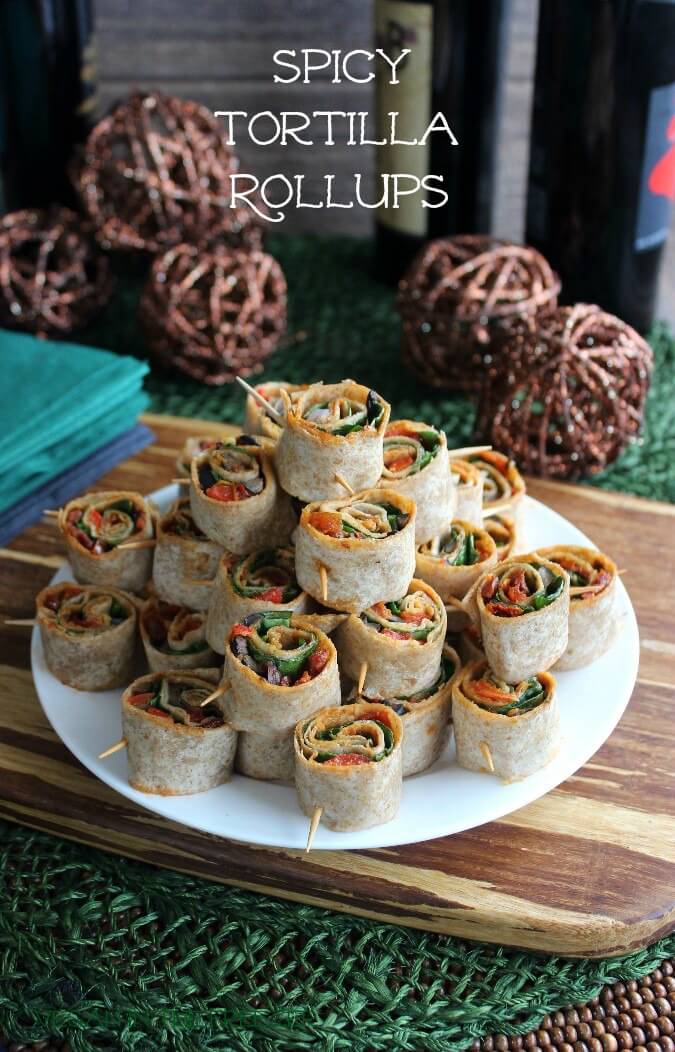 Spicy Tortilla Rollups are stacked as a pyramid surrounded with dark earthy background colors and different bottles of Tobasco flavors.