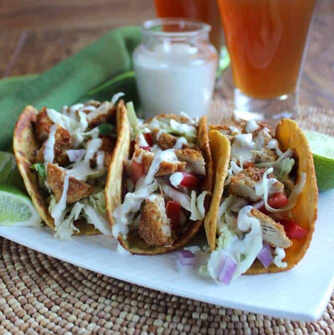 Three tacos lined up side by side on a white plate.