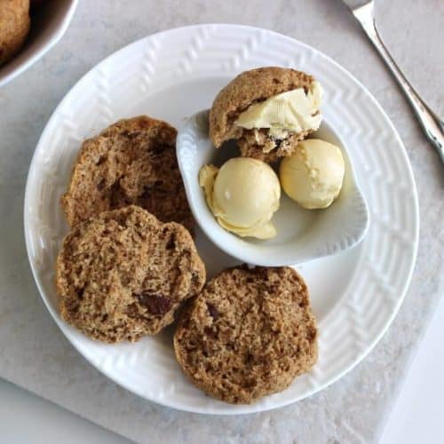 Overhead view of two dark bown scones with one open. They're on a small white plate with balls of dairy free butter.