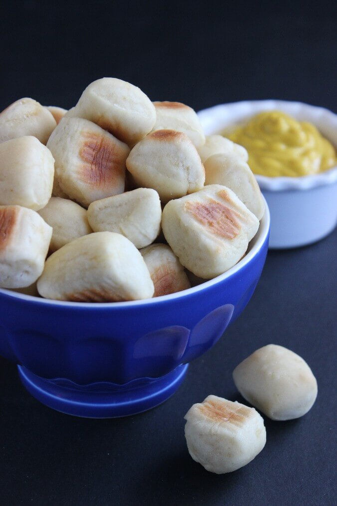 Fat Little Soft Pretzel Bites are overflowing in a cobalt blue bowl with yellow mustard in a bowl on the side.