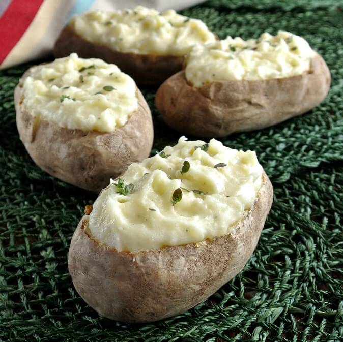 Twice Baked Potatoes are sitting on a green mat. There are four of them all stuffed and inviting.