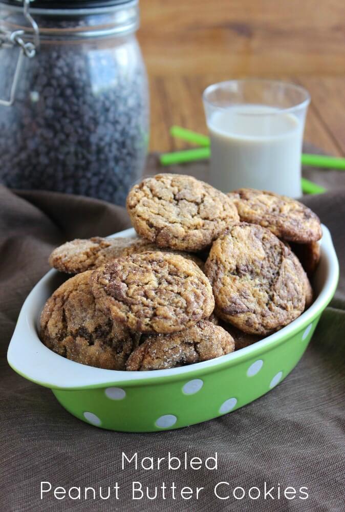 A bowlful of cookies is sitting in front of a jar of chocolate chips and a glass of dairy free milk.
