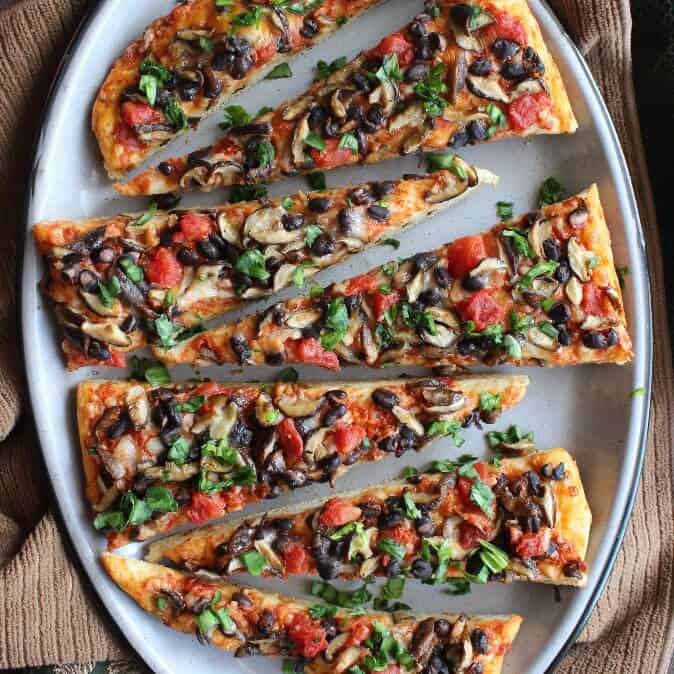 A close up photo of an oval mushroom pizza sliced diagonally on an enamelware platter.