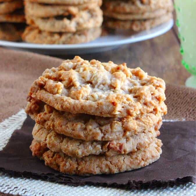 Apple Pie Cookies are stacked four high and sit on a chocolate colored napkin and beige burlap.