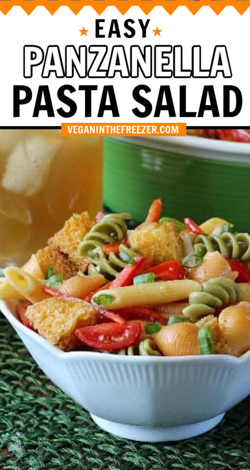 A white bowl full of cool colorful pasta and bread croutons on a green mat.