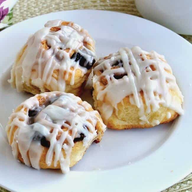 Three mini cinnamon rolls on a white plate against a woven straw background.