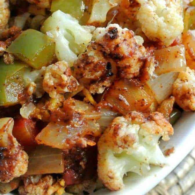 Close up photo of cooked cauliflower, onions and green bell peppers with lots os spices mixed through.