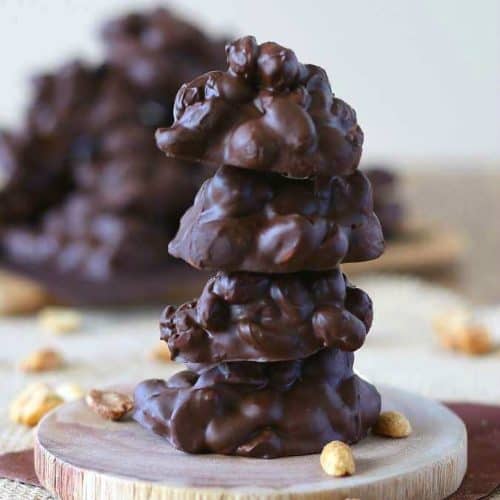 Slow Cooker Chocolate Clusters are stacked 4 high with more piled behind.