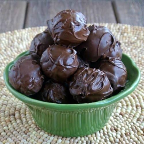 Chocolate covered balls are piled high in a green flared bowl in a wooden bead mat.