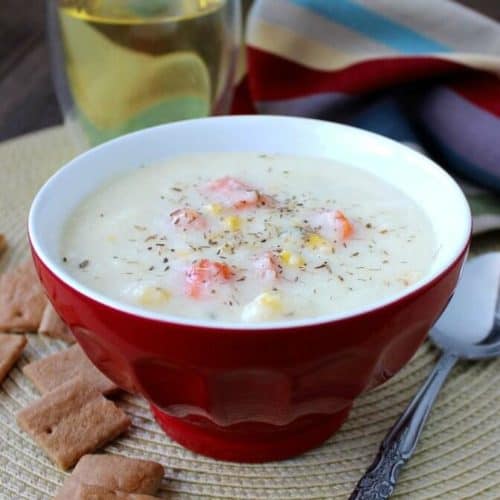 Creamy white Cauliflower Soup is in a red bowl with carrots and corn showing on the surface.