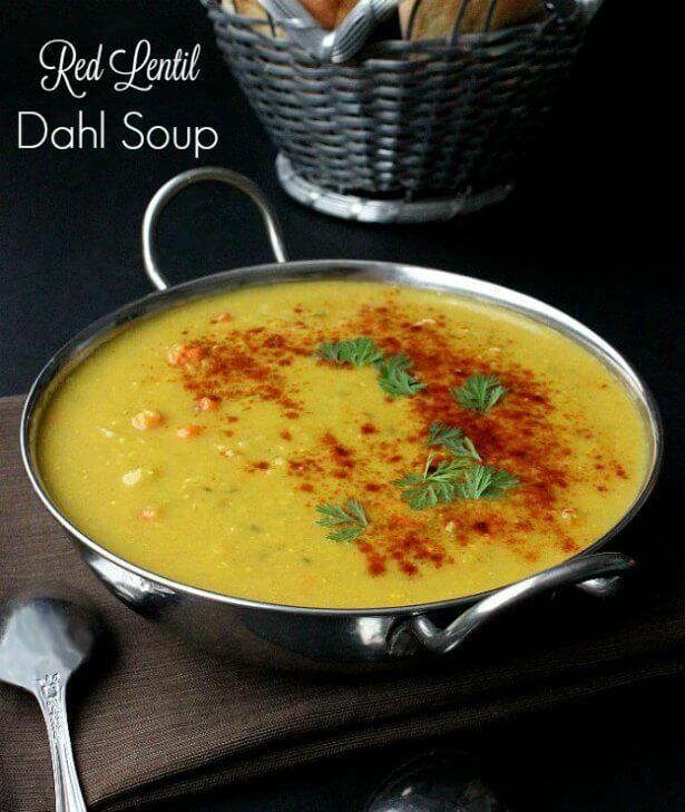 The rich yellow soup has red paprika and fresh green herbs sprinkled in an arc.