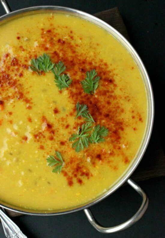 The rich yellow lentil soup has red paprika and fresh green herbs sprinkled in an arc.