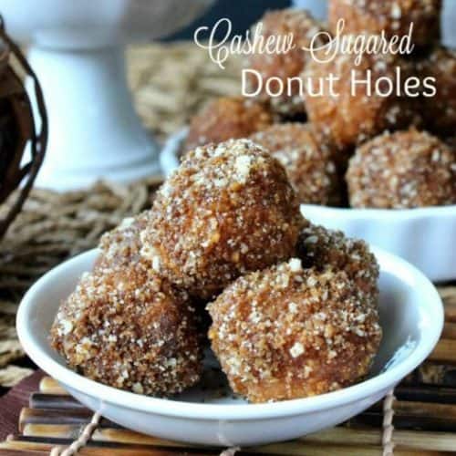 Cashew Sugared Donut Holes are five deep in a mini white bowl. Crumbly cashew sugar is all over these little bites and the are also sitting on a bamboo mat.