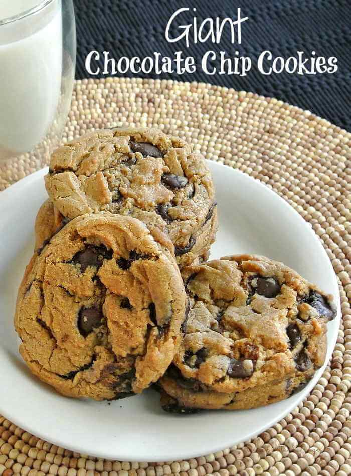 Five giant chocolate chip cookies spred and piles on a white plate.