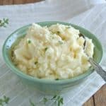 Creamy mashed potatoes are in a green bowl with thyme sprinkled on top with a spring on the side.